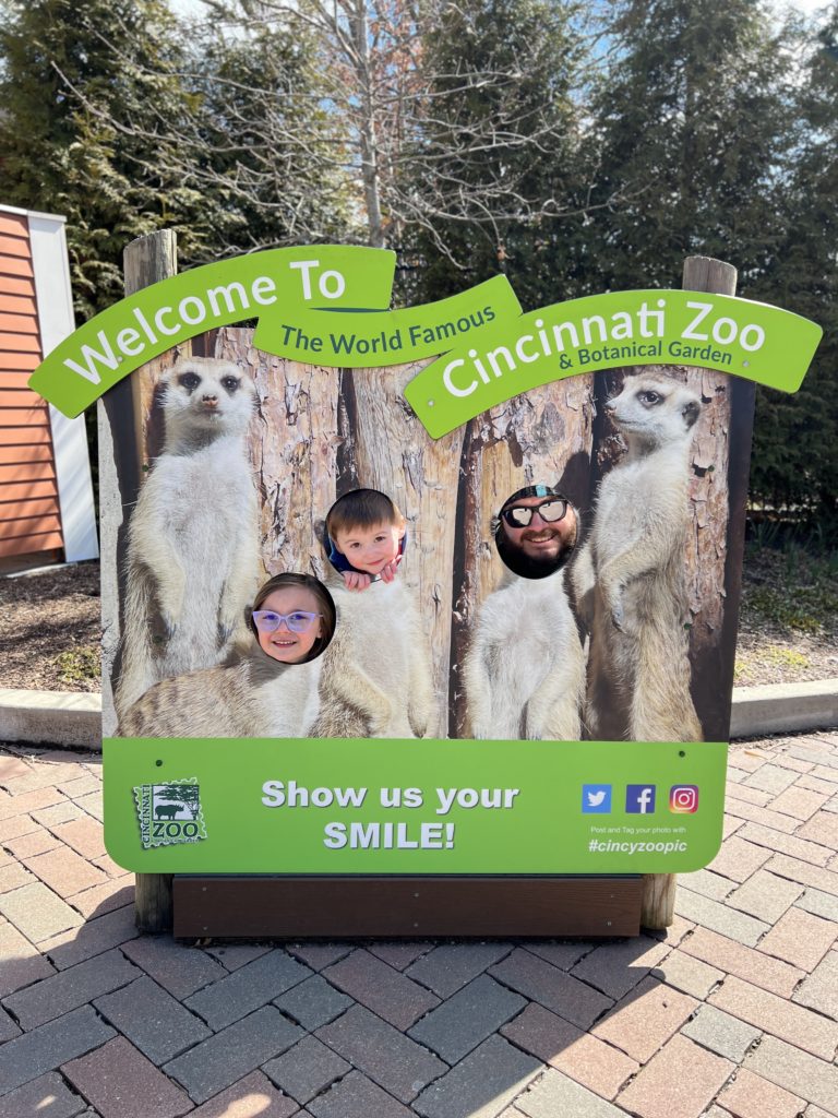 Two young kids and their father in a hole-photograph pretending to be meerkats.