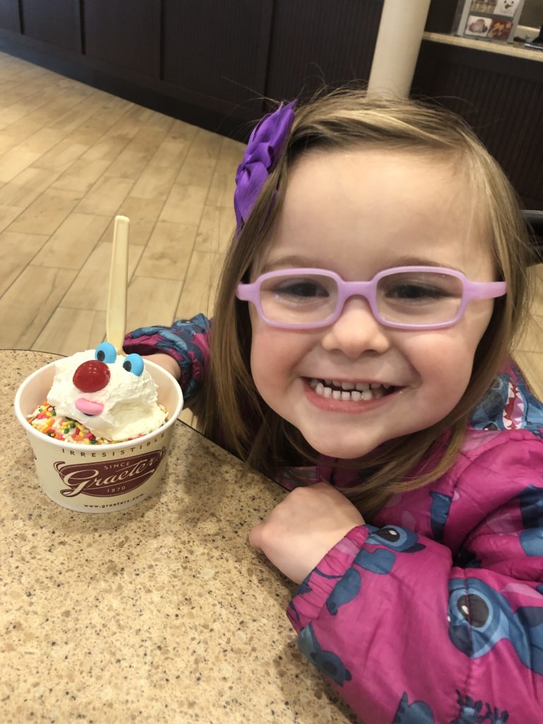 Young girl with an ice cream sundae on the table in front of her. 